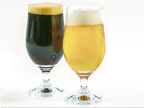 A glass of dark beer beside a glass of light beer, both topped with foam, against a white background