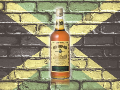 A bottle of Old Jamaica rum standing in front of a brick wall painted with the Jamaican flag