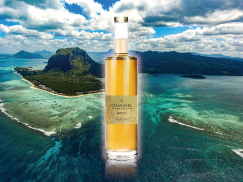 A bottle of Chamarel Premium Rum Gold standing above an aerial view of Mauritius's mountains and turquoise coastline