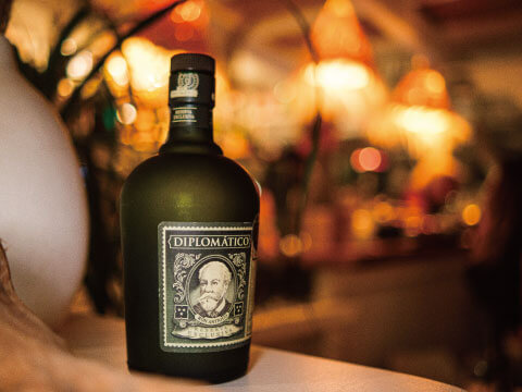 A dark green bottle of Diplomático Reserva Exclusiva rum on a bar counter with warm bokeh lighting in the background