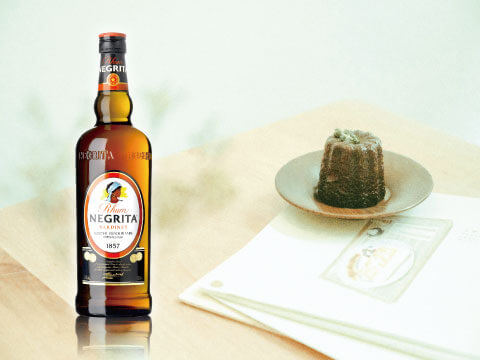 A bottle of Rhum Negrita standing on a wooden table next to a small rum-soaked cake on a plate