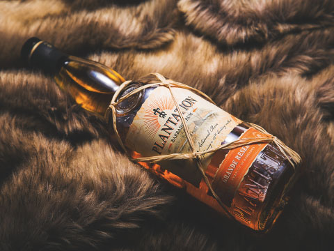 A bottle of Planteray Original Dark rum lying diagonally on a soft brown fur textile