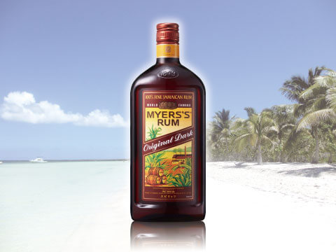 A bottle of Myers's Rum Original Dark standing on a white sand beach with palm trees and turquoise water