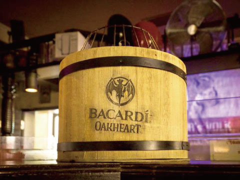 A wooden barrel stamped with the Bacardí bat logo and "Oakheart" branding, sitting on a bar counter