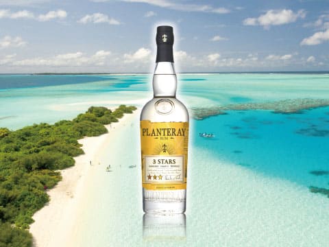 A bottle of Planteray 3 Stars white rum standing above an aerial view of a turquoise Caribbean beach and reef