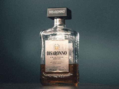 A bottle of Disaronno Originale amaretto liqueur standing against a solid teal-colored background
