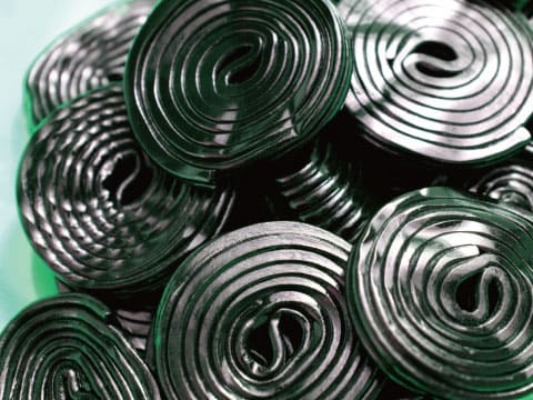 A pile of coiled black licorice candy wheels sits stacked together.