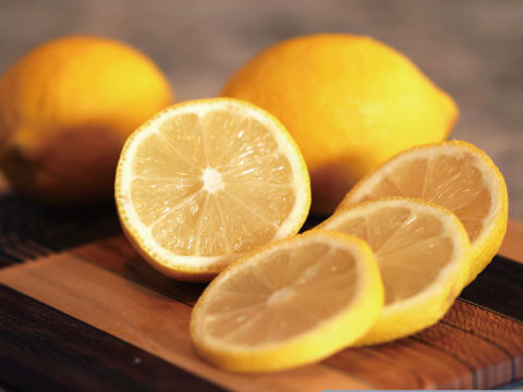 Whole lemons and freshly cut lemon slices arranged on a wooden cutting board