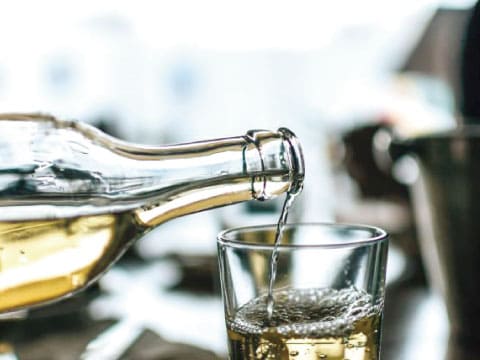 White wine being poured from a bottle into a glass, with bubbles visible in the liquid