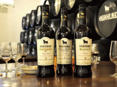  Three bottles of Osborne sherry — Pedro Ximénez, Santa María Cream, and Bailén — displayed on a wooden bar counter with tasting glasses