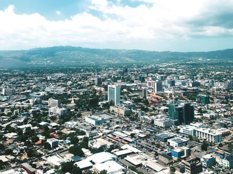 An aerial view of Kingston, Jamaica's cityscape with high-rise buildings, spread out beneath distant mountains