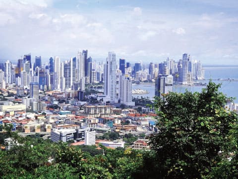 A view of Panama City's modern skyline with dense high-rise buildings along the coast, framed by green foliage