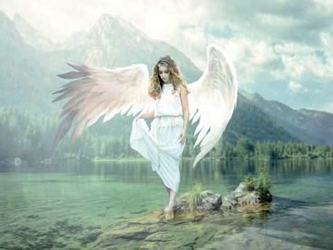 Woman dressed as an angel with large feathered wings standing on rocks by a lake, mountains and forest in the background