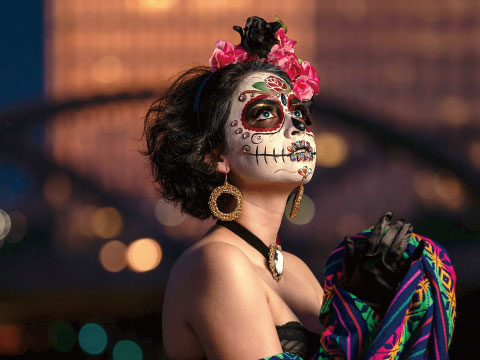 A woman with traditional Día de los Muertos sugar skull face paint and floral headpiece, referencing the calavera imagery on Espolón's tequila label