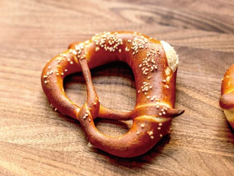 A freshly baked pretzel with a golden-brown crust and coarse salt, sitting on a wooden cutting board