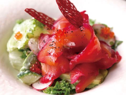 A smoked salmon appetizer garnished with salmon roe, radish, and mixed greens, topped with a crispy beet chip