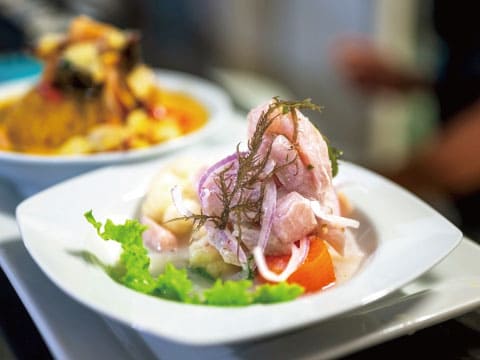 A white plate of fish ceviche marinated with red onion and herbs, garnished with lettuce, served on a restaurant table
