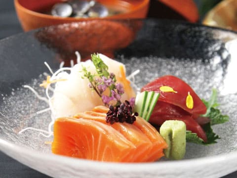 A ceramic plate of assorted sashimi including salmon, tuna, and squid, garnished with edible flowers and wasabi