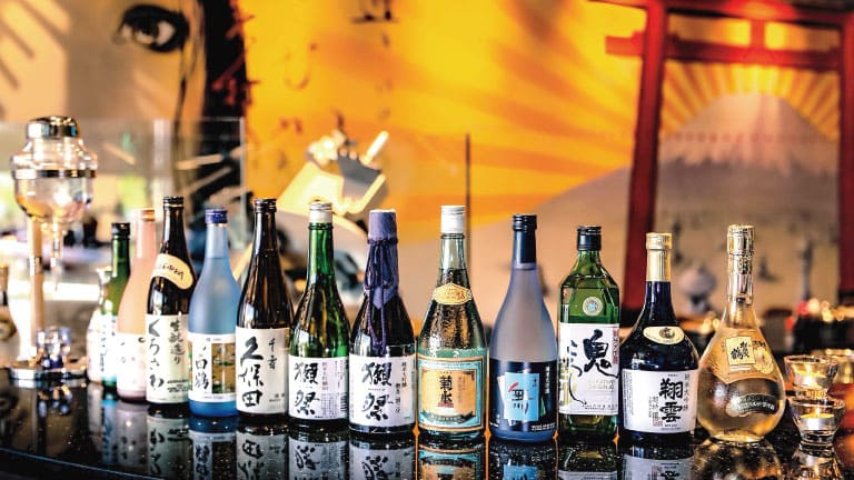 A lineup of various Japanese sake bottles with colorful labels displayed on a bar counter