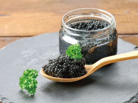 Black caviar in a glass jar and heaped on a wooden spoon, garnished with fresh parsley on a slate board