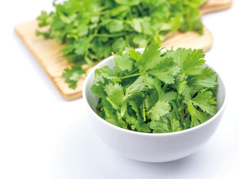 A bowl of fresh cilantro leaves sits in front of more cilantro on a wooden cutting board.