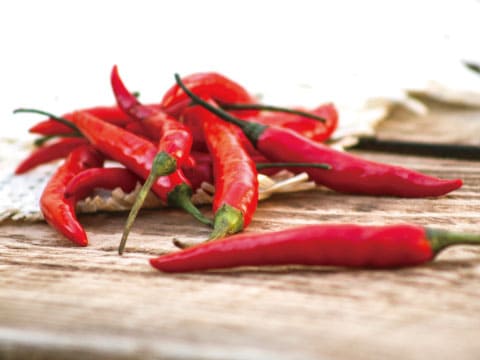 A pile of fresh red chili peppers with green stems arranged on a rustic wooden surface