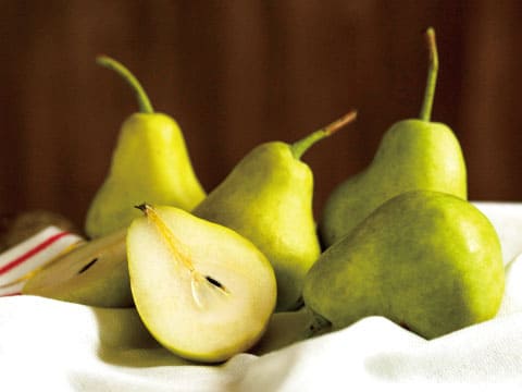 Whole green pears and a halved pear showing its core, arranged on white linen
