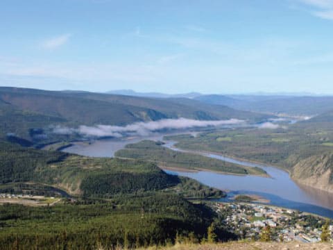 Aerial view of the Yukon River winding through forested hills near Dawson City, Canada, with morning mist over the water