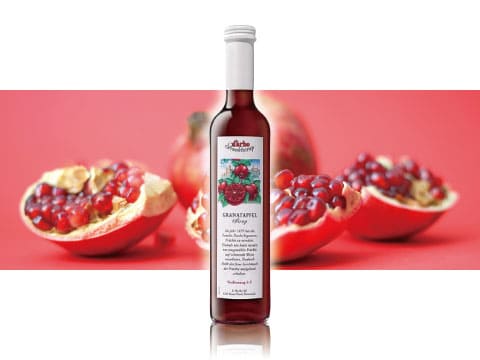 A bottle of Darbo grenadine syrup standing between halved pomegranates against a red background