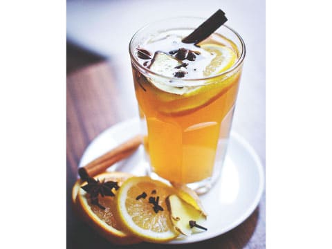 A glass of grog cocktail garnished with orange and lemon slices, cinnamon sticks, star anise, and whole cloves on a plate