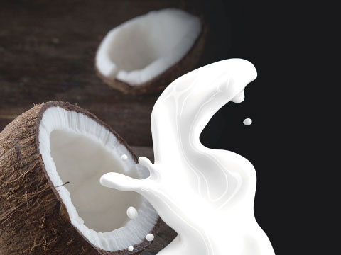 A dramatic splash of coconut milk beside two halved coconuts on a wooden surface