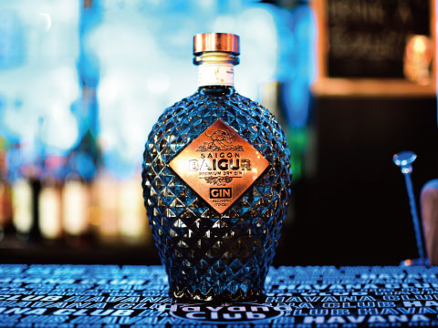 A bottle of Saigon Baigur premium dry gin with a diamond-textured glass design, standing on a patterned bar counter