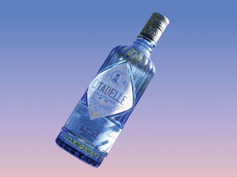 A bottle of Citadelle gin tilted against a blue-to-pink gradient background