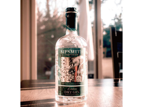 Bottle of Sipsmith London Dry Gin with a green label on a wooden table beside a sunlit window