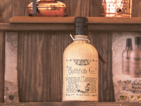 Bottle of Bathtub Gin wrapped in brown paper and tied with string, displayed on a wooden bar shelf