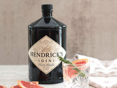 Black bottle of Hendrick's Gin next to a glass garnished with grapefruit slices and a rosemary sprig on a marble surface