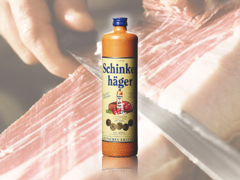 A bottle of Schinkenhager gin superimposed against a background of thinly sliced cured ham being carved