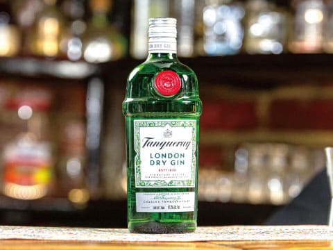 A bottle of Tanqueray London Dry Gin standing on a bar counter, with blurred liquor bottles in the background