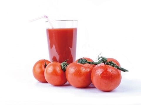 A glass of tomato juice with a straw, surrounded by fresh whole tomatoes with stems, on a white background