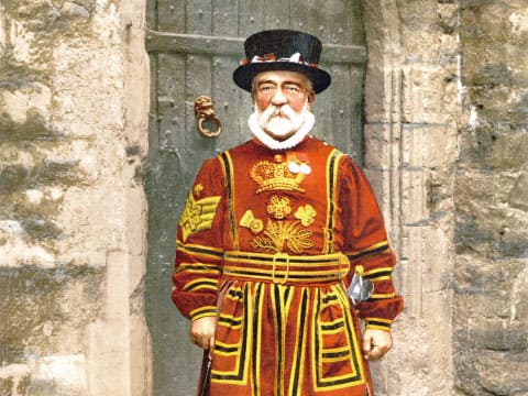 A colorized historic photograph of a Yeoman Warder in traditional Tudor-style red and gold state dress, standing before a stone archway at the Tower of London