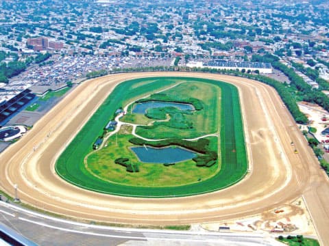 Aerial view of Aqueduct Racetrack in Queens, New York, showing the oval dirt track, green infield with ponds, and surrounding neighborhood