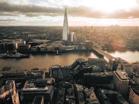 An aerial view of London's Southwark district at sunset, with the Shard skyscraper and the River Thames visible below dramatic clouds