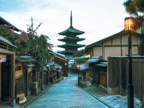 Stone-paved lane lined with traditional wooden buildings and glowing lanterns, leading to a five-story pagoda at dusk in Kyoto
