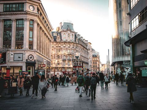 Crowd of pedestrians walking along a busy city street lined with classic stone buildings and modern glass buildings