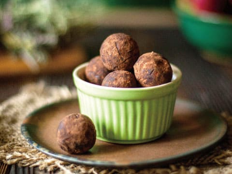 Cocoa-dusted chocolate truffles piled in a green ceramic bowl, with one truffle resting beside it on a plate