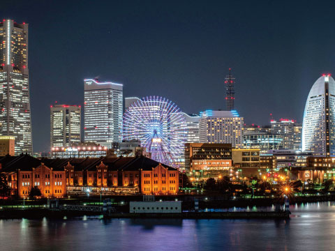 Nighttime skyline of Yokohama, Japan, featuring the illuminated Cosmo Clock Ferris wheel and Minato Mirai skyscrapers reflected on the water