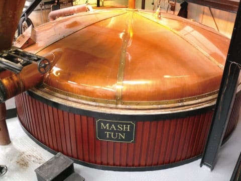 Copper-domed mash tun with wooden cladding at a whisky distillery, where ground malt is mixed with hot water to turn starch into sugar