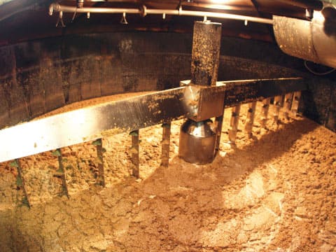 Inside a mash tun, rotating rakes stir a thick mash of ground malt and hot water to extract sweet wort during the saccharification stage of whiskey production