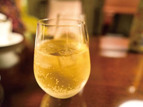 Sparkling golden ginger ale with ice in a stemless glass on a warm wooden café table