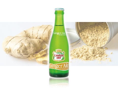 Green bottle of Canada Dry Ginger Ale, the original dry-style ginger ale, in front of fresh ginger root and ginger powder